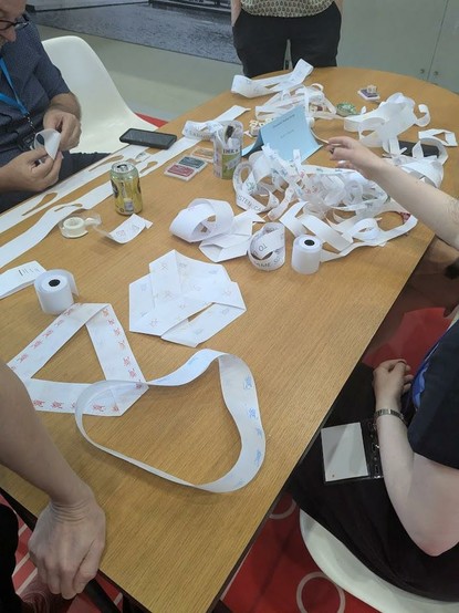 A table covered with various paper crafts, including long strips of paper, some folded into geometric shapes like a Mobius strip.