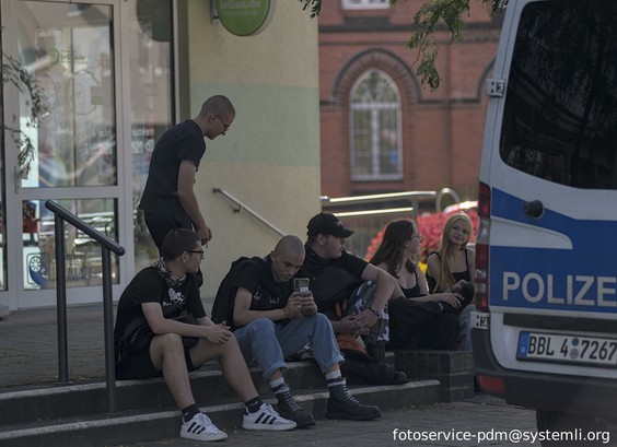 6 jungnazis sitzen auf einer treppe und beobachten die csd parade