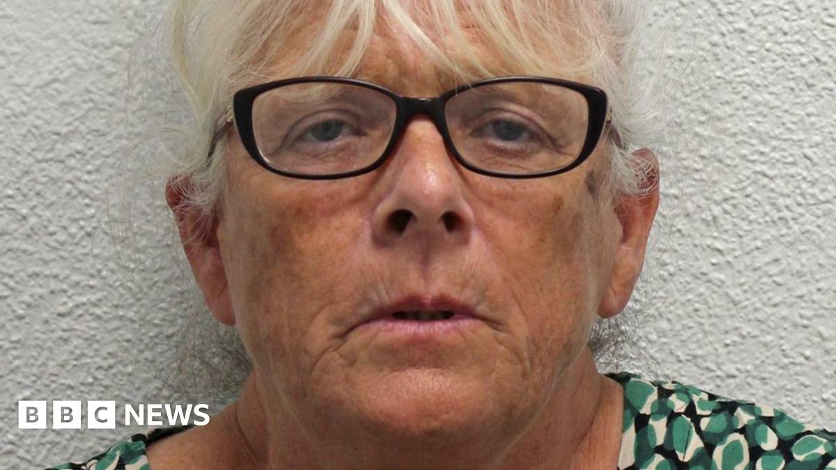 Deborah Mason, a woman with white hair and wearing dark rimmed glasses. She is standing against a white background and wearing a green, white and black patterned top