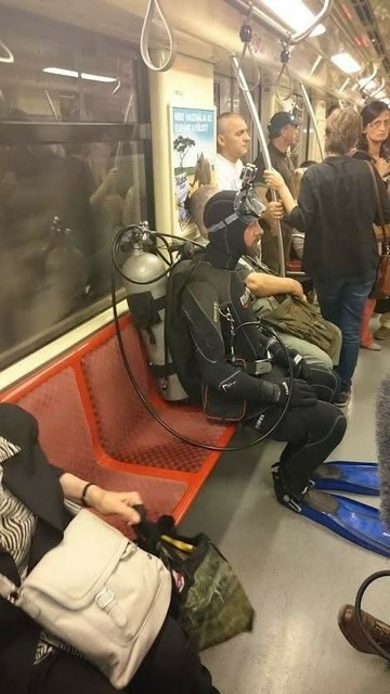 Hombre vestido con todo el equipo de submarinista sentado en un vagón de metro 